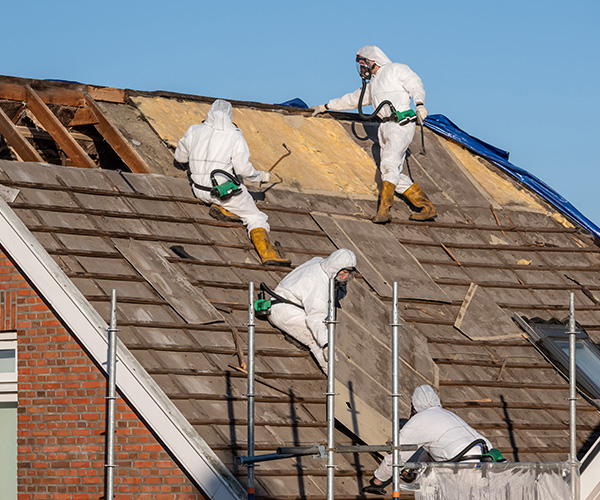 Three asbestos removal staff in PPE working on roof